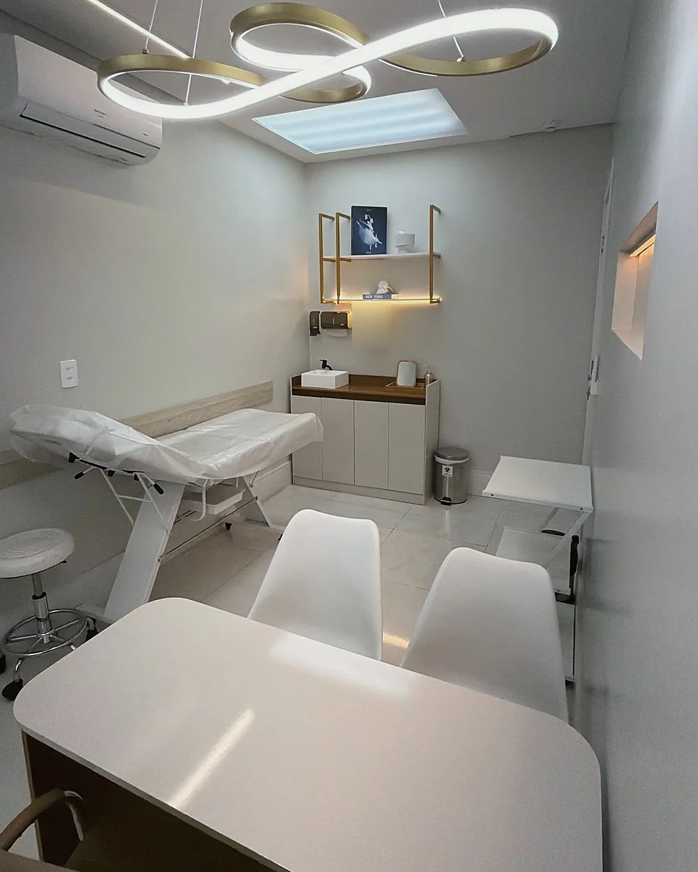 Sala de procedimentos da clínica, com maca e luminária dourada