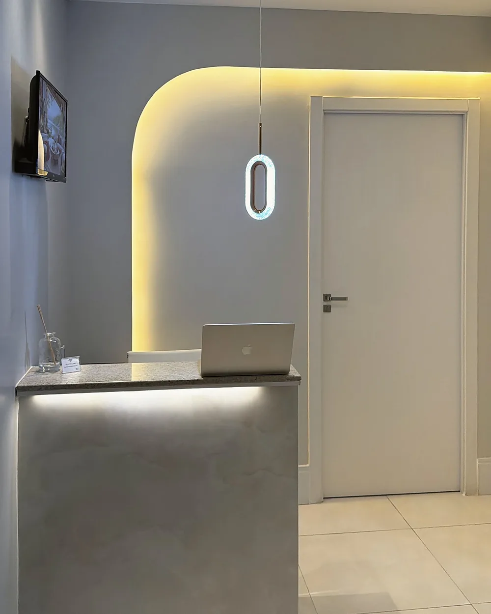 Recepção da clínica, com balcão claro e parede em arco iluminada por luz dourada