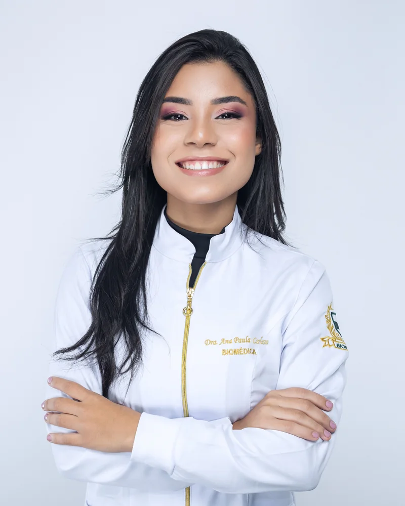 Dra. Ana Paula Carlesso sorrindo, de jaleco e com os braços cruzados
